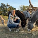 Frau hockt vor vier Eseln auf der Weide des Rietzer Bergs.